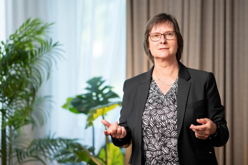 Petra Borchardt spricht und gestikuliert vor einem hellen Hintergrund