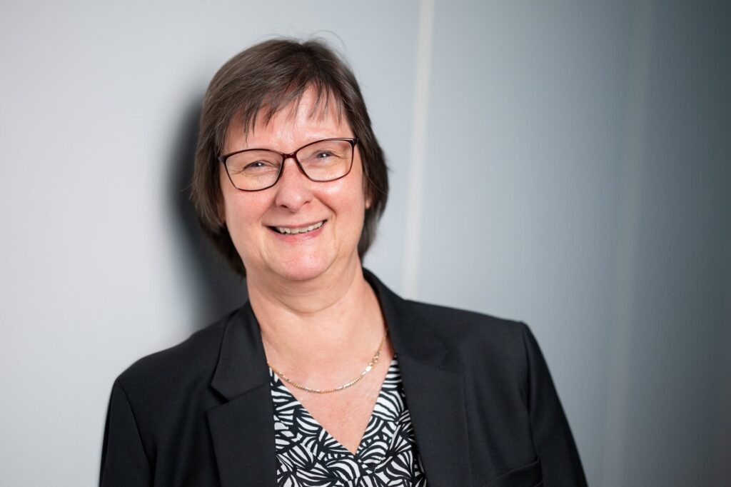 Petra Borchardt lächelnd vor einer hellen Wand.