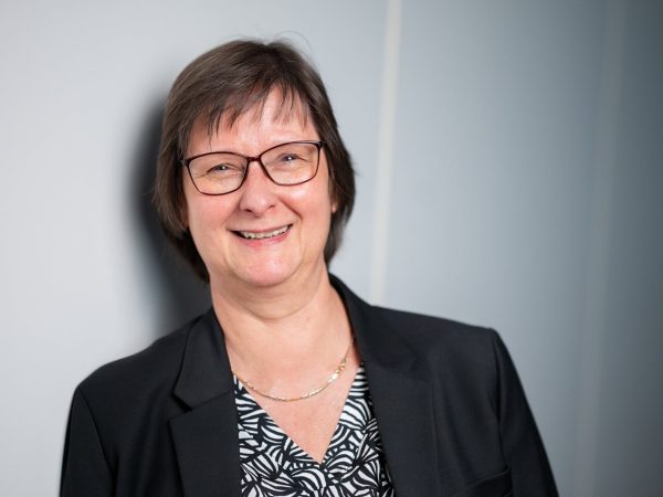 Petra Borchardt lächelnd vor einer hellen Wand.